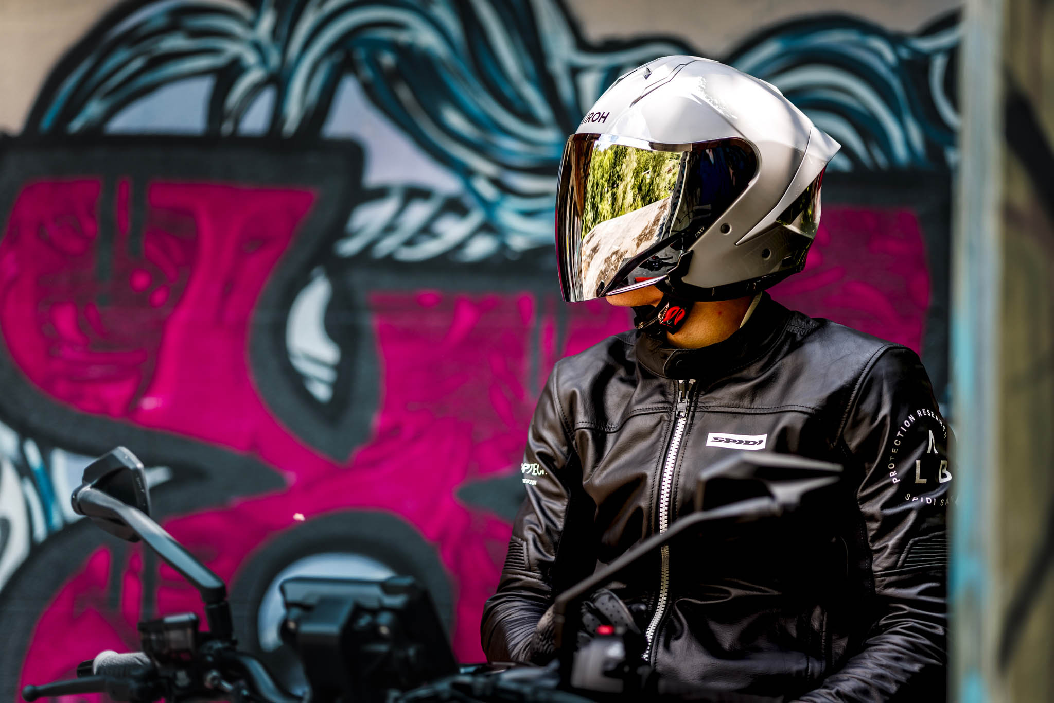 Motard portant le casque jet AIROH H.21 blanc avec visière miroir devant un mur graffiti