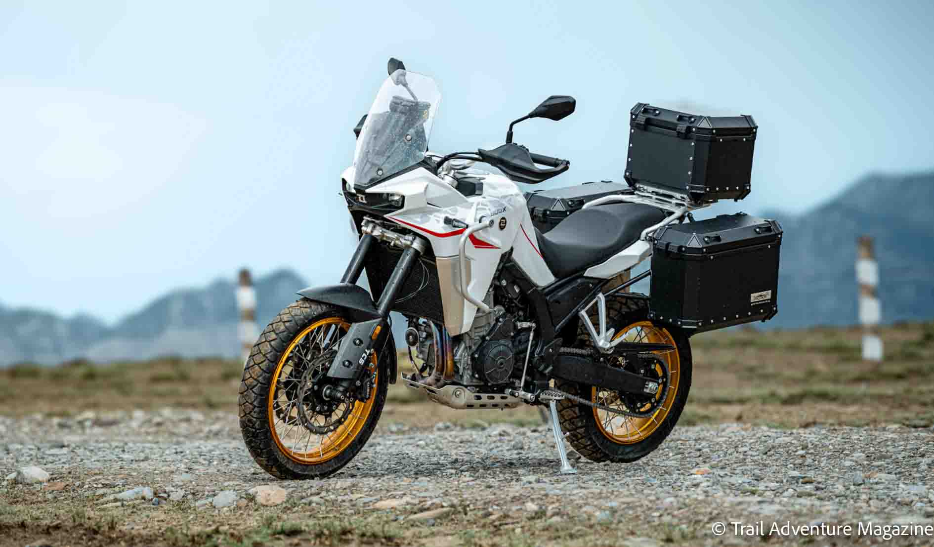 Moto trail équipée de valises latérales et de crash bars posée sur une piste tout-terrain